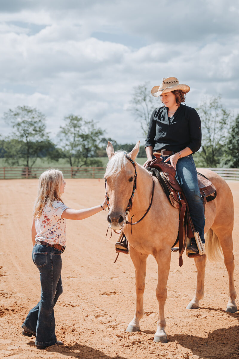 Meg teaching a young rider in the arena alongside a palomino horse