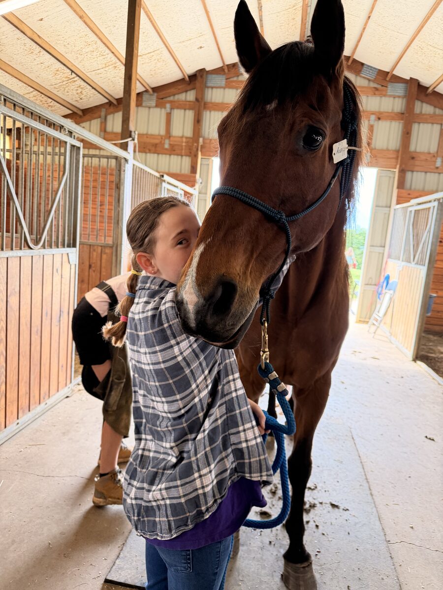 A young rider leading a horse through the barn aisle at Gracewood Acres